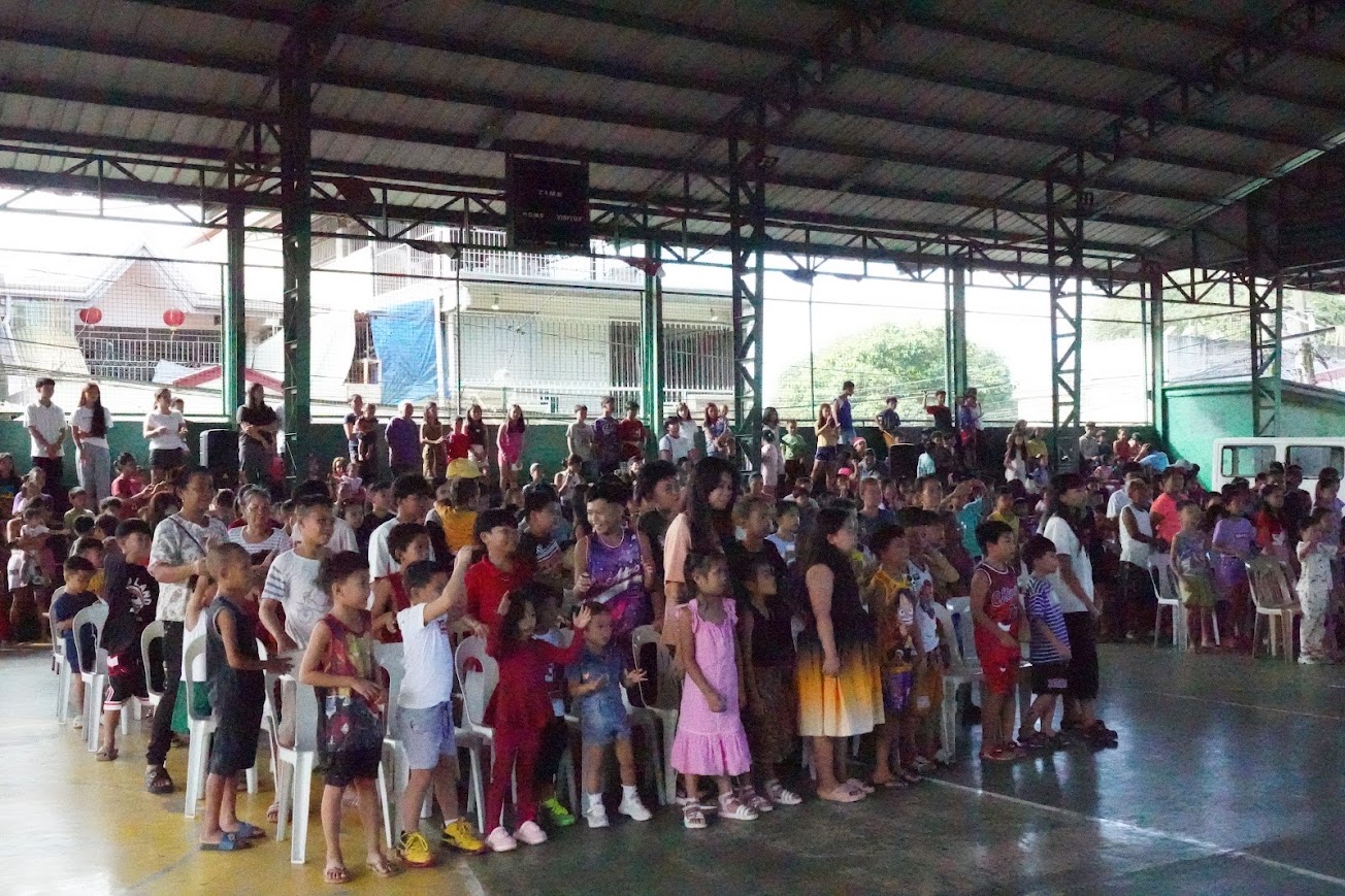 Children in the front rows with hands raised, families behind.