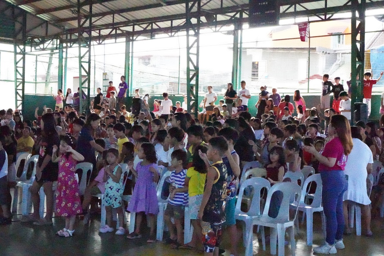Children fill the court for the morning session, seated on the floor and in chairs.
