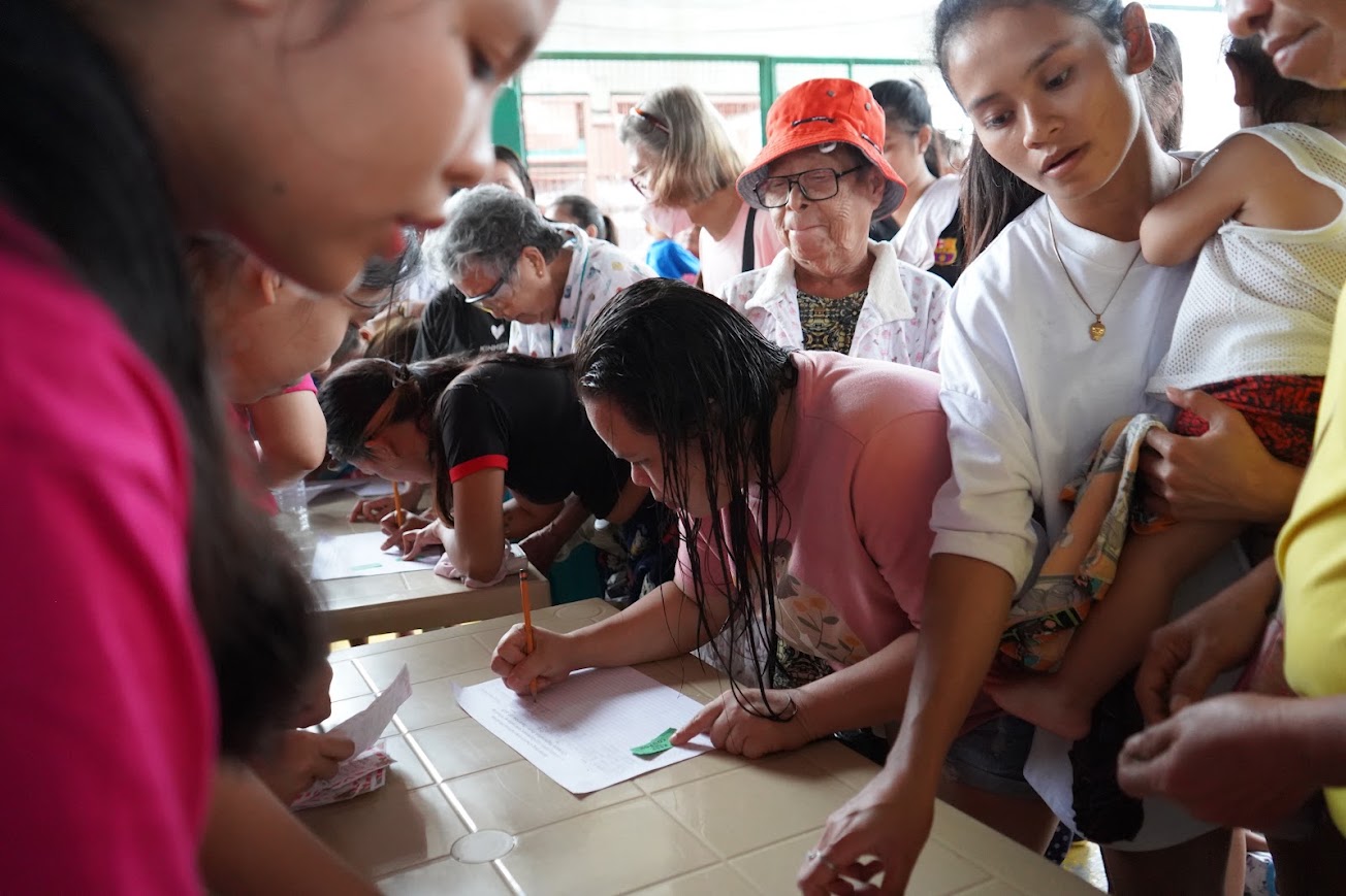 Registration — families lean over the sign-in sheets as a team member checks names.