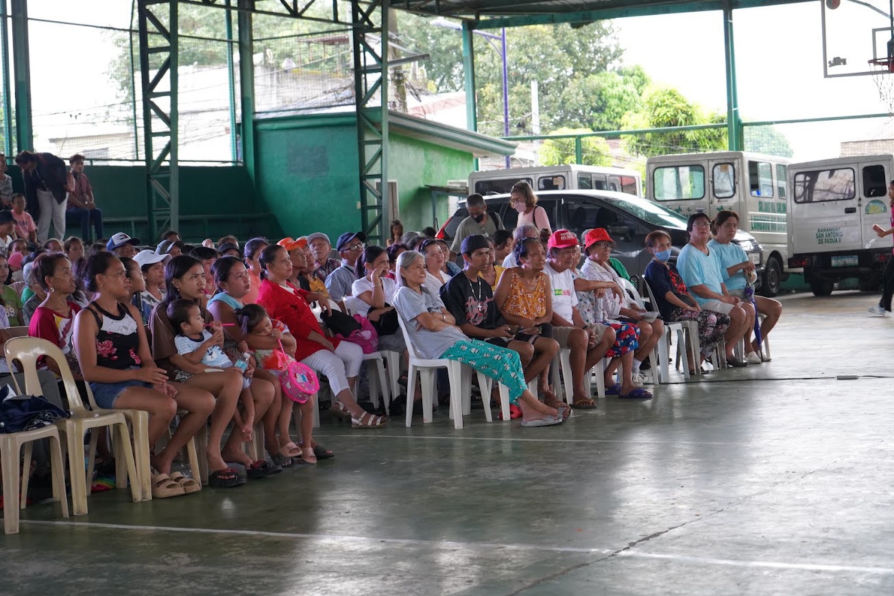 The crowd seated and waiting, jeepneys parked along the far side.