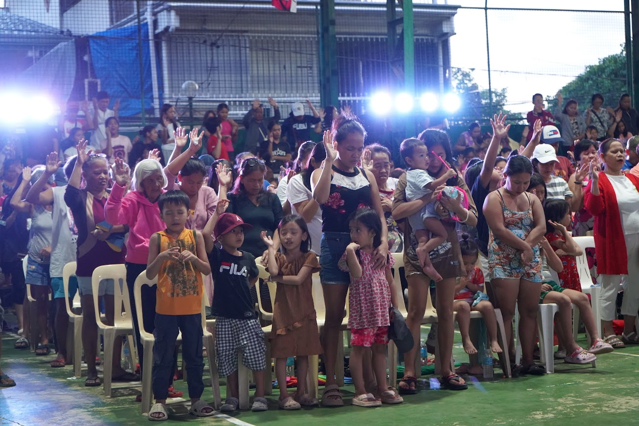Community members standing with hands raised as the stage lights come on.