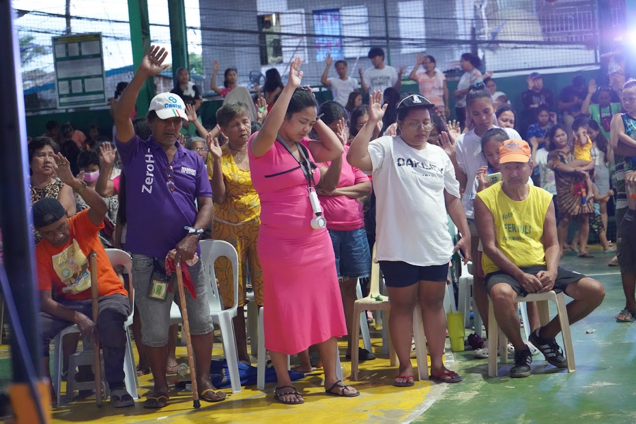 Children and mothers with hands lifted in the front rows.