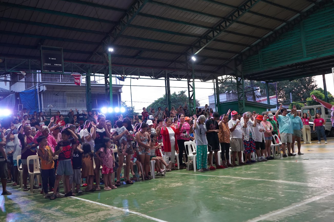 A team member leads the opening prayer at the mic, the team standing behind.
