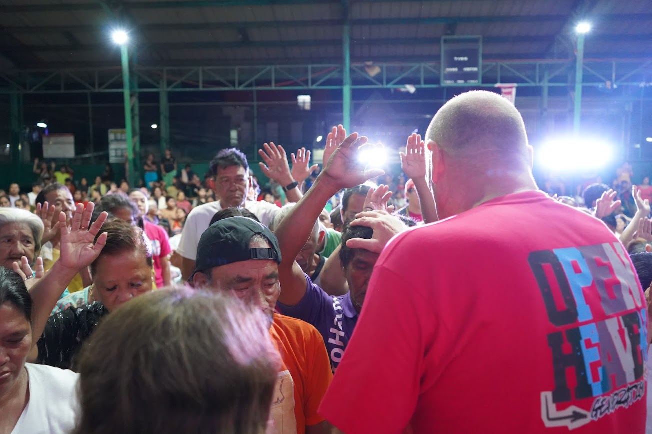 A team member lays a hand on a man's head, hands raised behind.