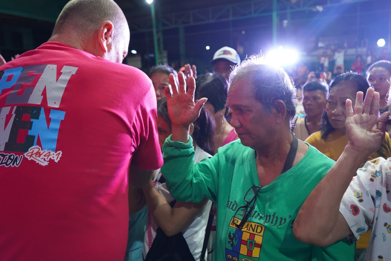A team member prays over a man in the crowd, his hands lifted.
