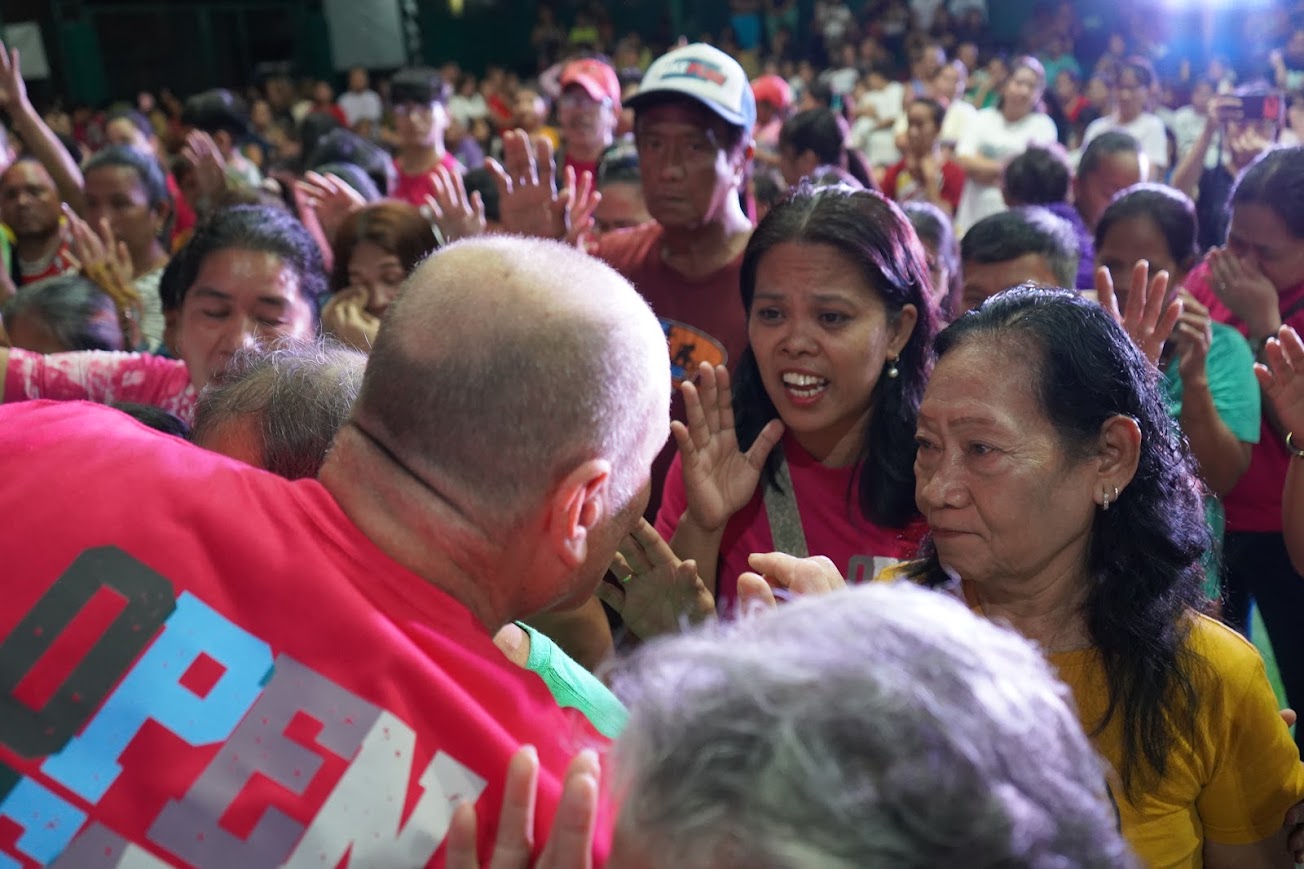A team member leans in toward two women, hands lifted around them.