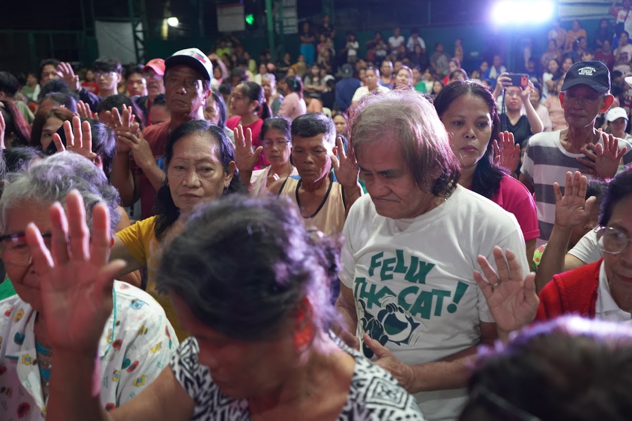 Hands raised across the crowd, an elder in the foreground.