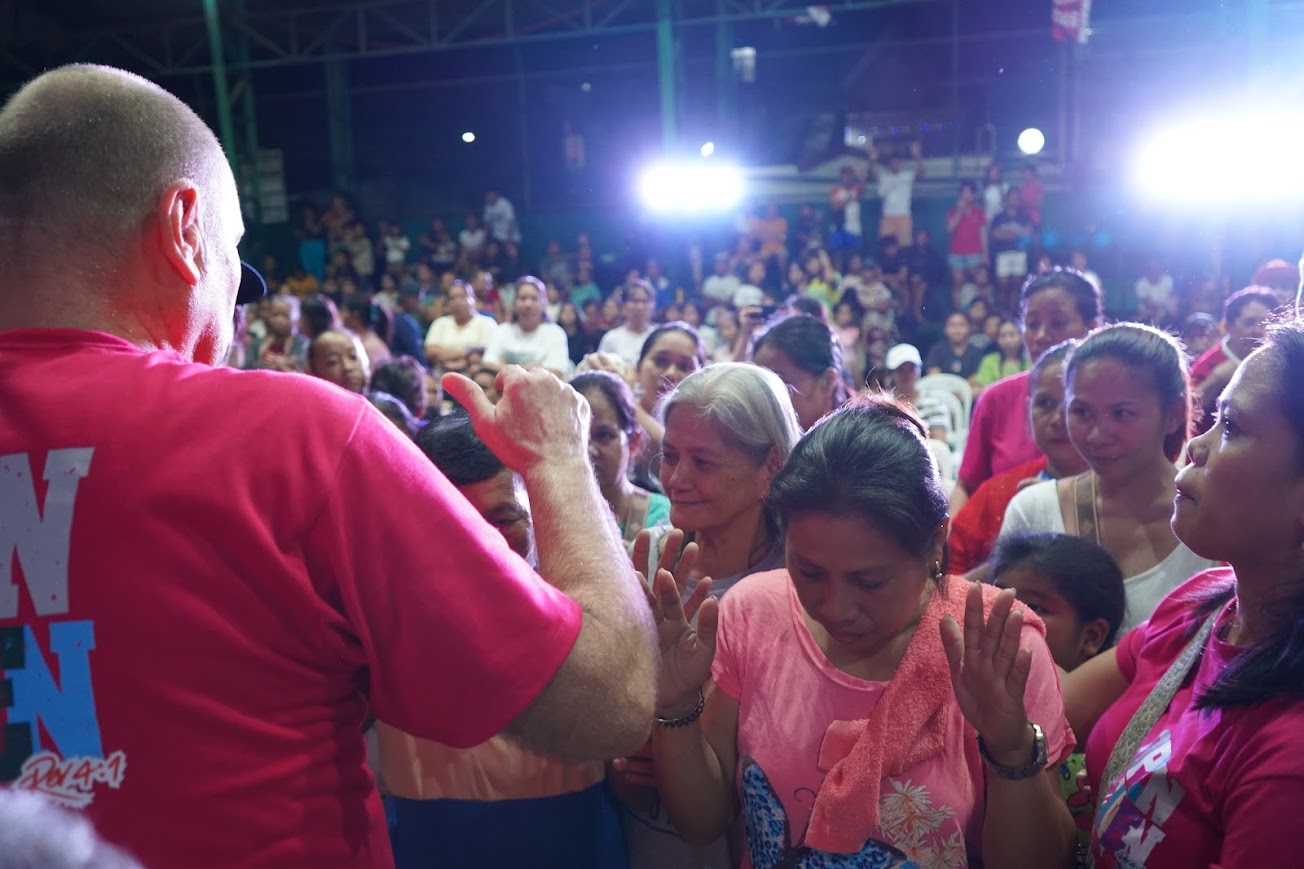 Hands laid on a woman's head as she prays, the crowd around her.