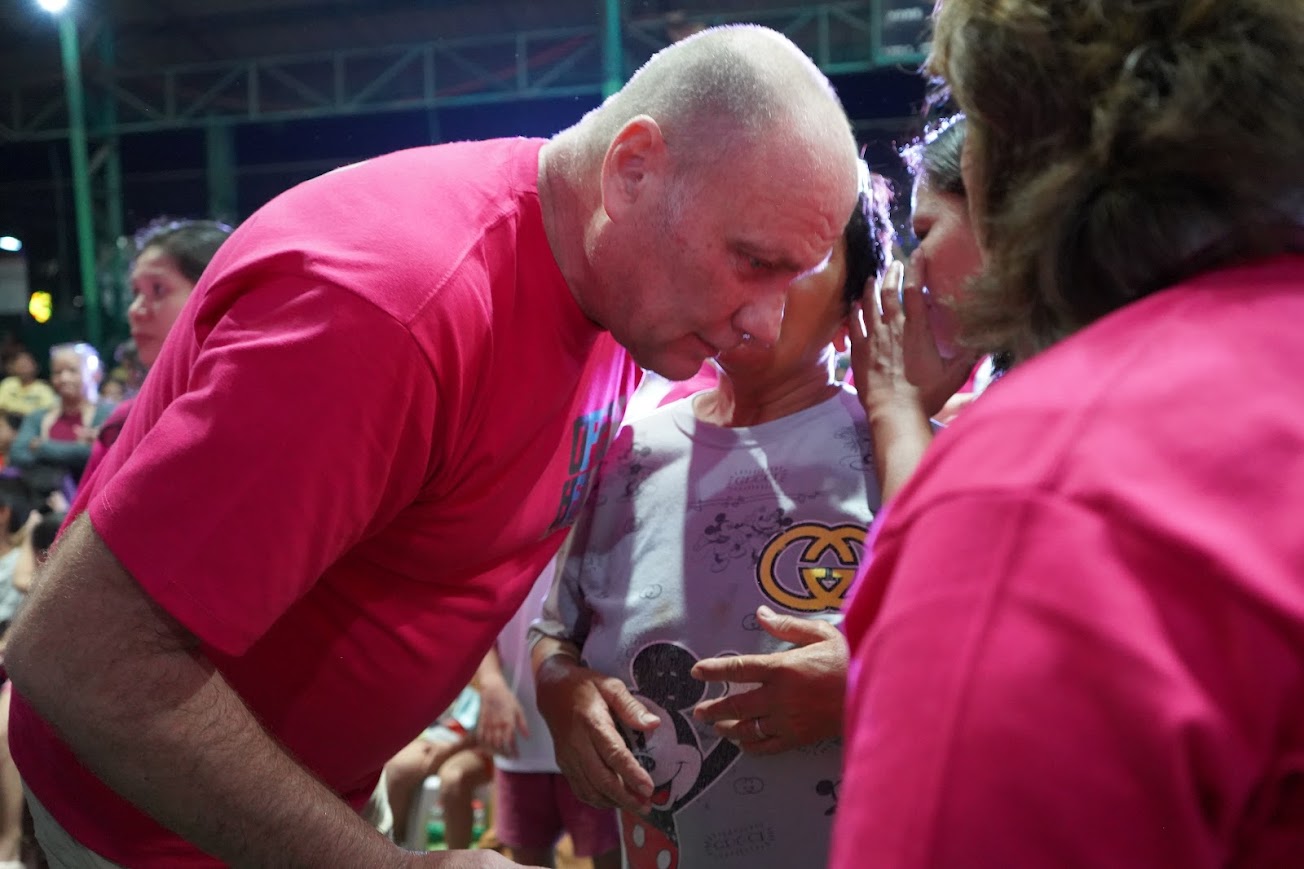 A team member leans in to pray with a woman, one hand at her shoulder.