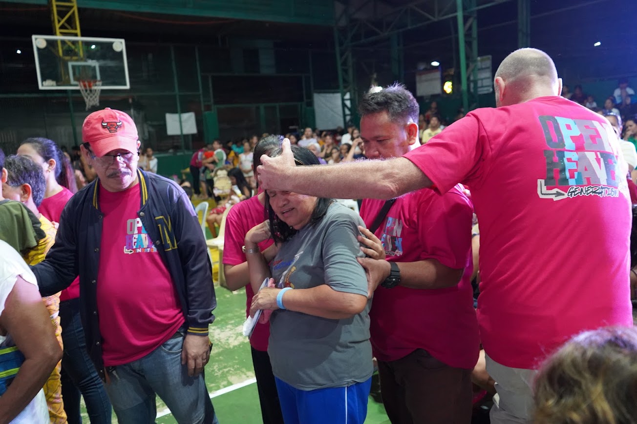Team members gather around a woman in prayer, hands on her shoulders.