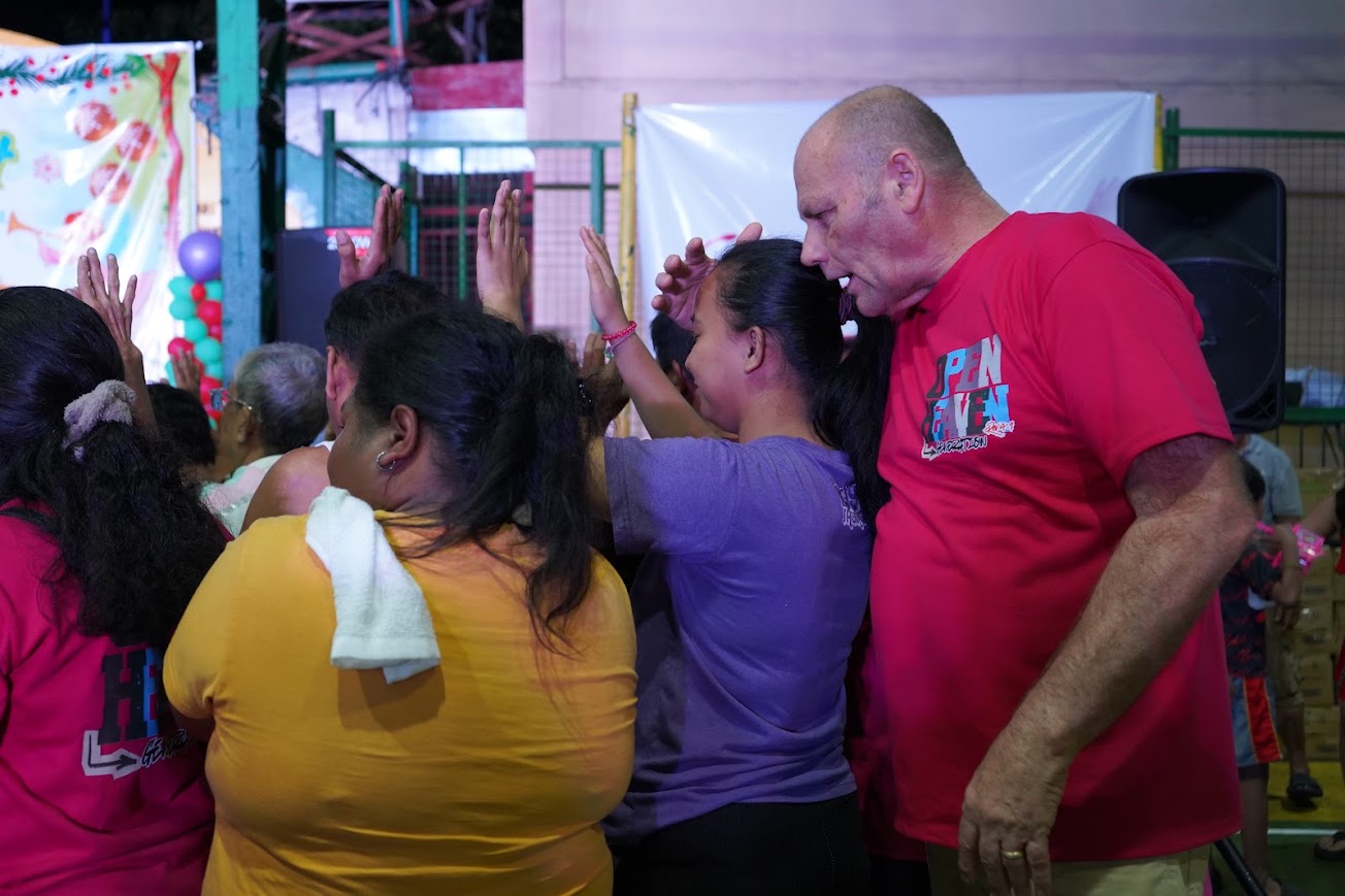 A team member lays a hand on a young woman's head, the nativity banner behind.