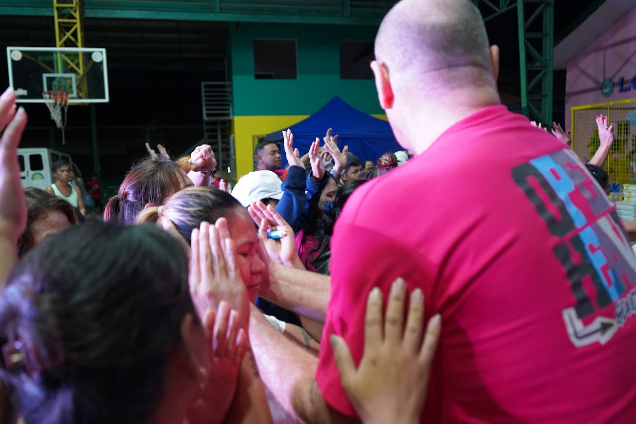 Hands cover a woman's face in prayer as a team member lays hands on her.