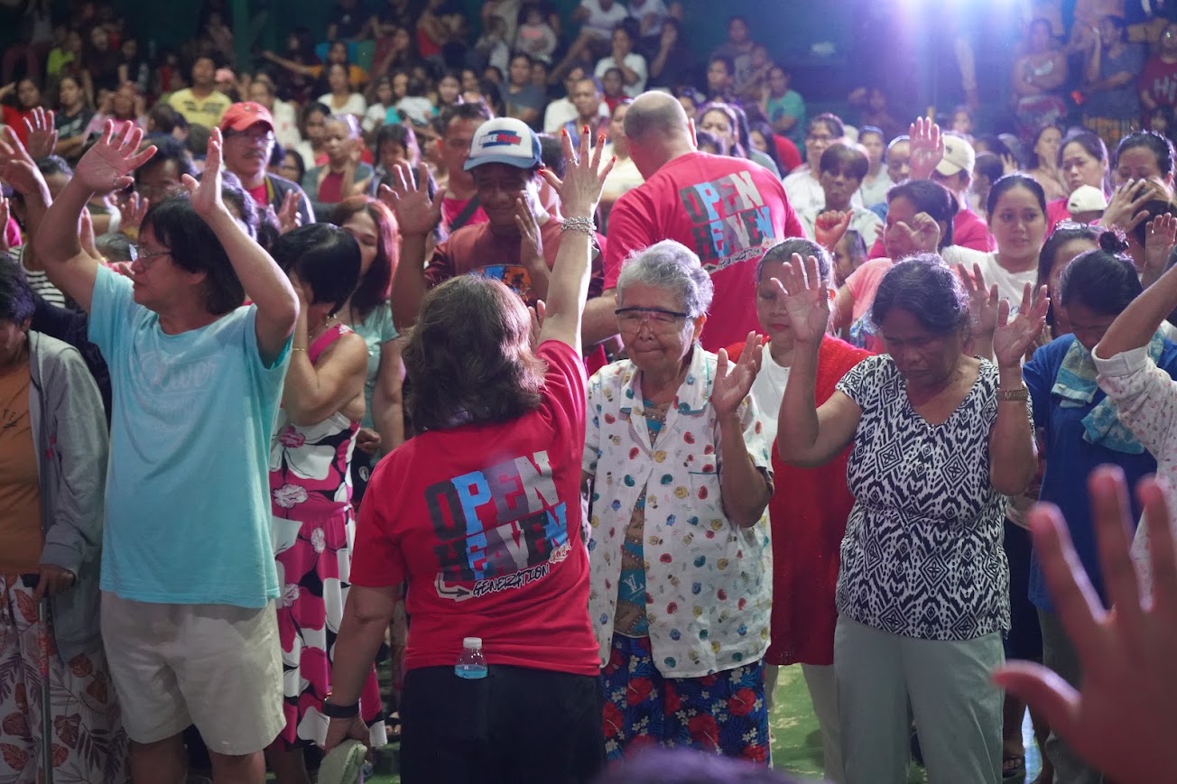 The team lays hands on community members as the band plays, hands lifted across the floor.