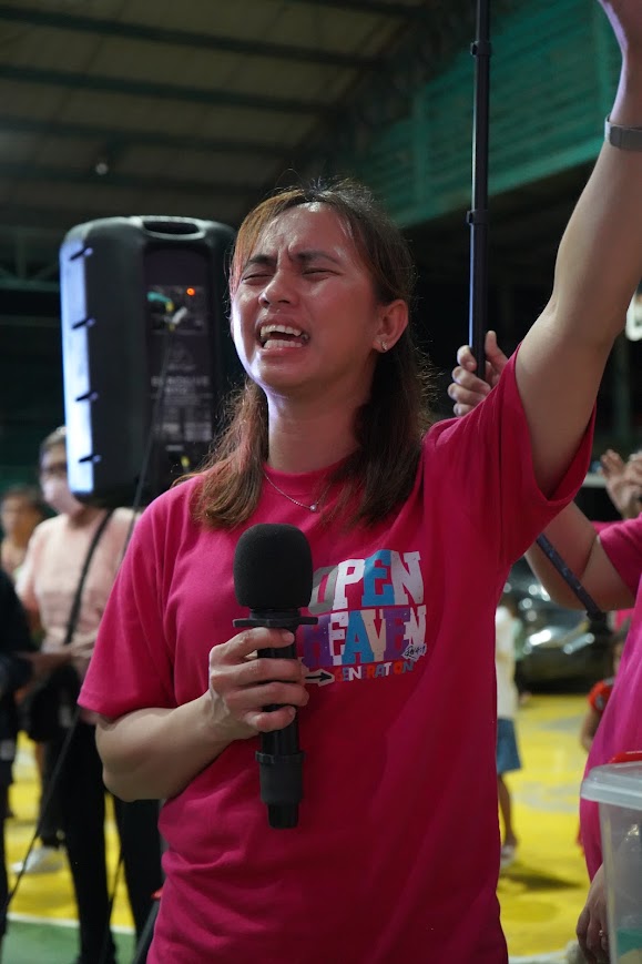 A team member sings with eyes closed and one hand raised under the court lights.