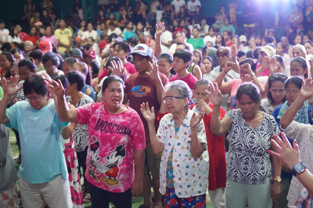 Hands raised across the crowd — elders in the front rows.