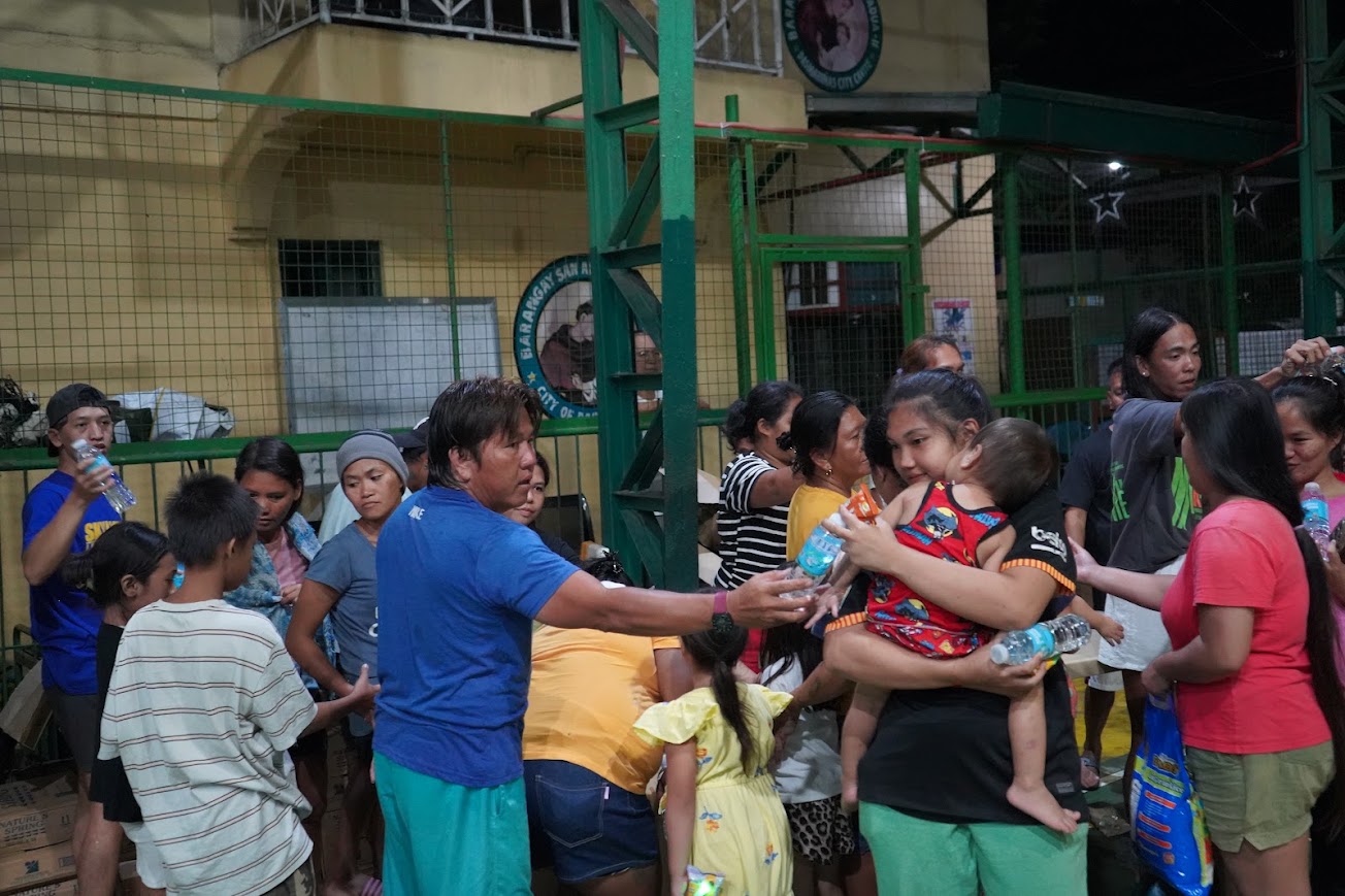A team member hands water to a mother carrying a child.