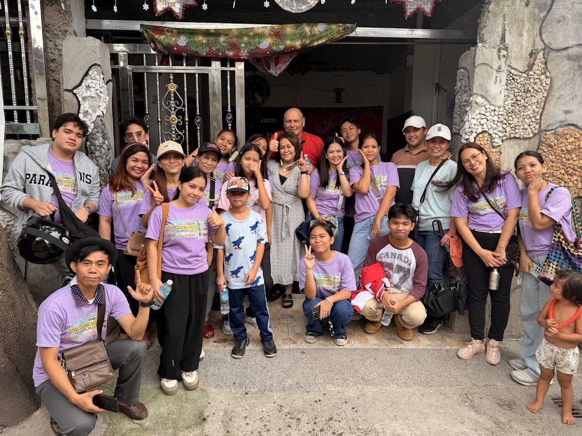 The team outside a family's home, a Christmas banner above the gate.
