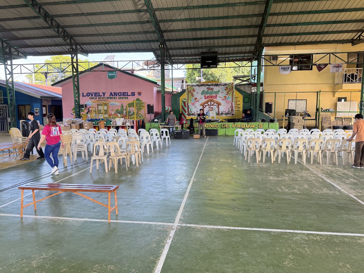 The empty court before the crowd — chairs in rows, the stage dressed, boxes of gifts stacked at the side.