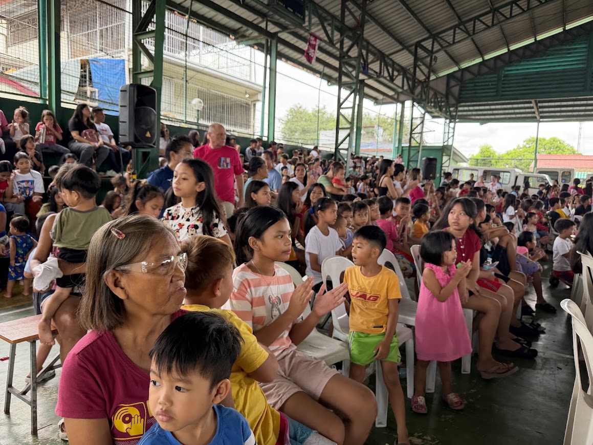 An elder with her grandchildren in the front row, children clapping beside her.