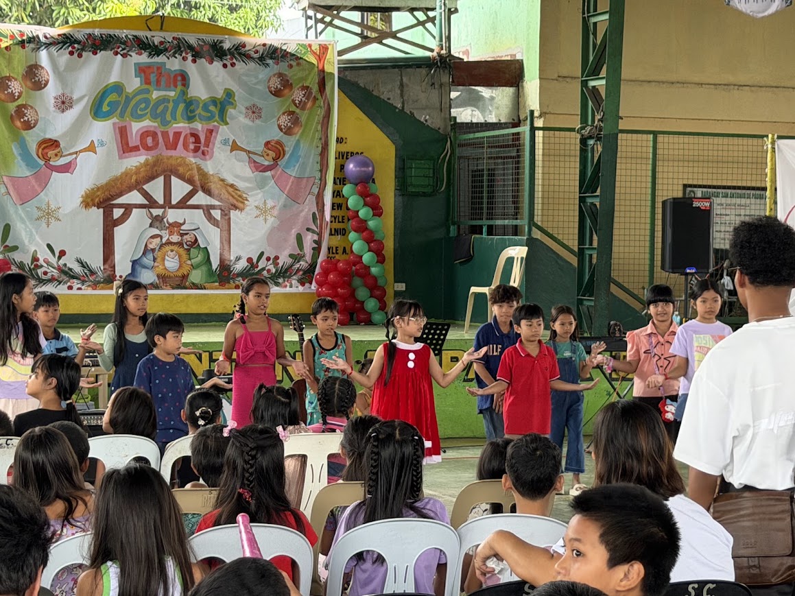 Children perform at the front beneath "The Greatest Love!" nativity backdrop.