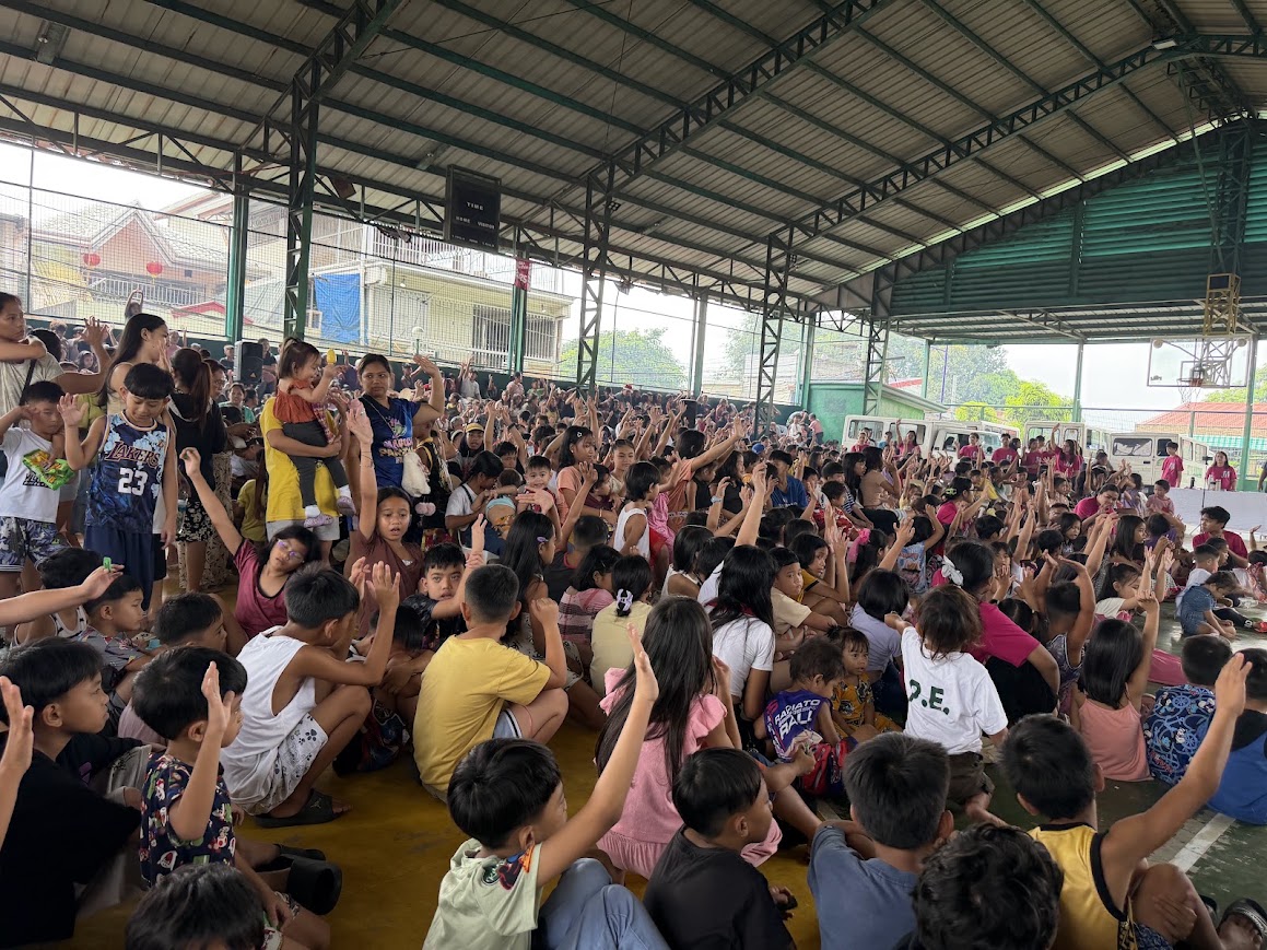 Hands go up across the court, mothers with infants at the edge.