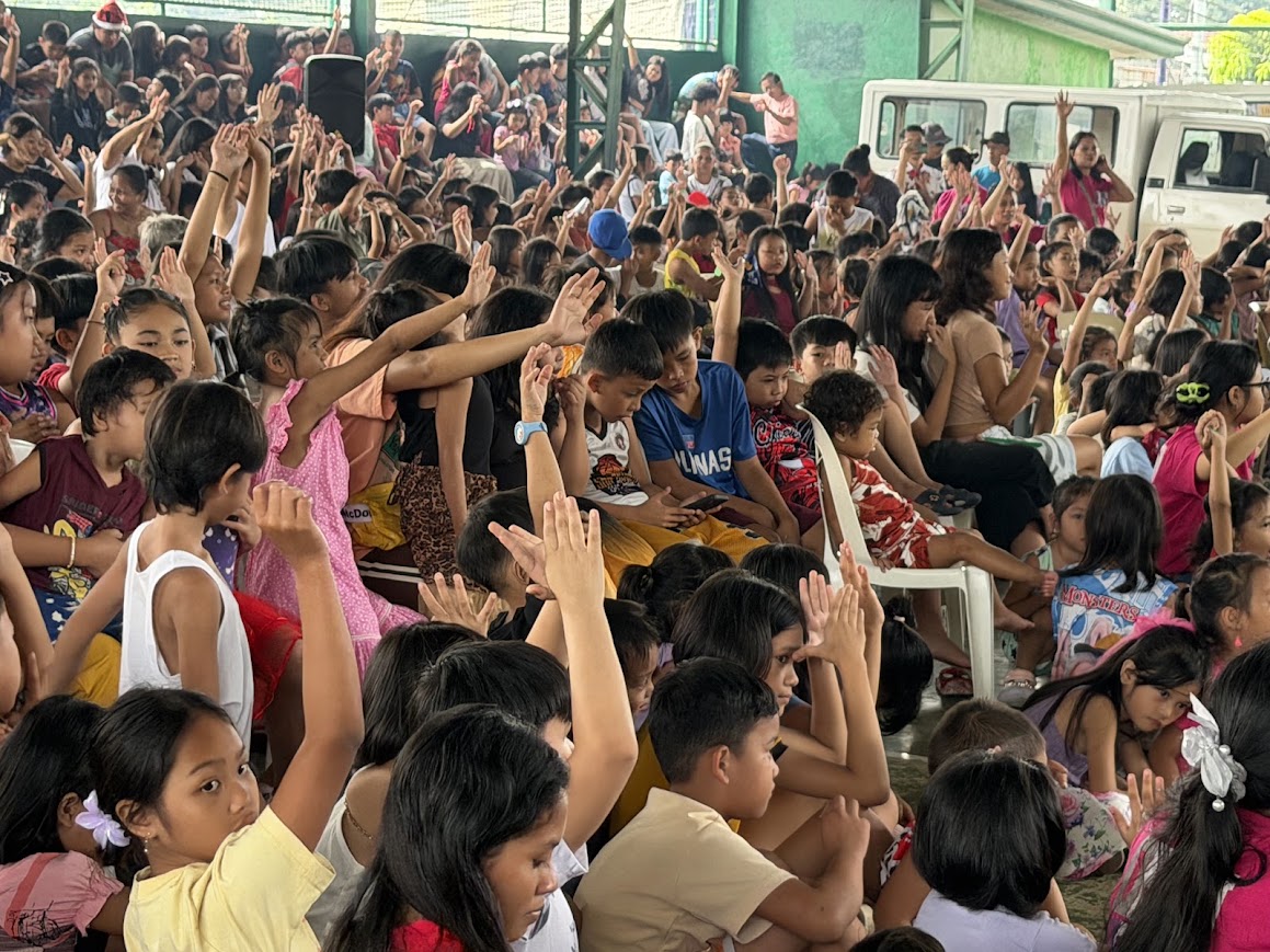 Hands raised — children turning toward the front.
