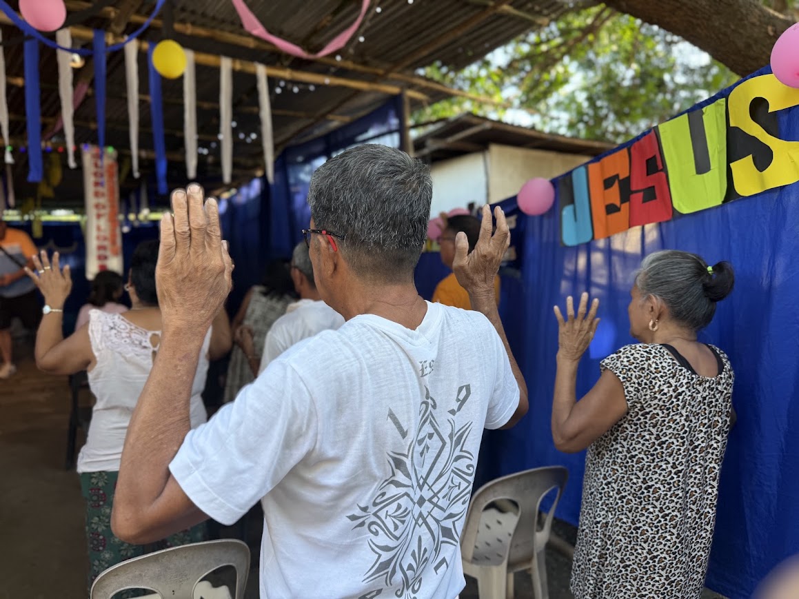 Community members join in prayer beneath the 'Jesus' banner.