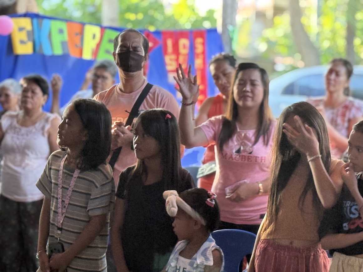 The congregation raises their hands together beneath the 'Jesus Experience' banner.