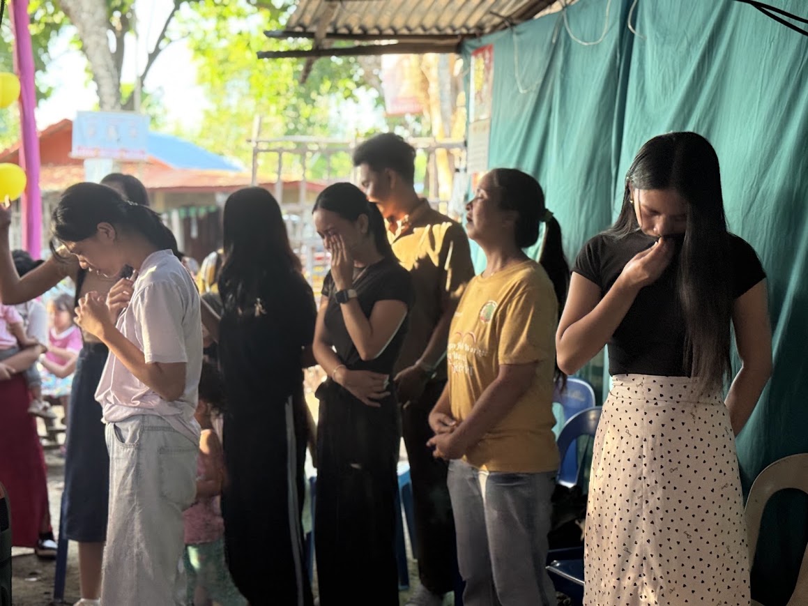 A line of young women bow their heads together in prayer.