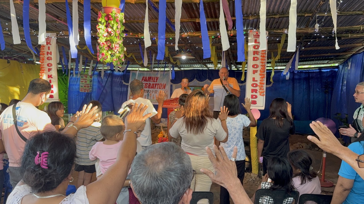 The congregation lifts their hands in worship beneath the string lights.