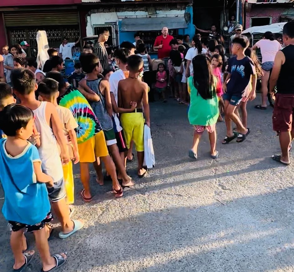 The line from behind — children queued along the street, the ministry leader at the far end.