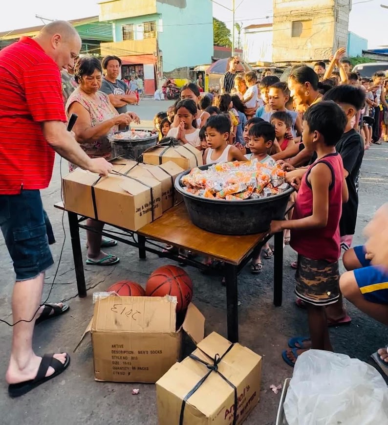 The leader opens the boxes as the first children reach the table, basketballs stacked beside it.