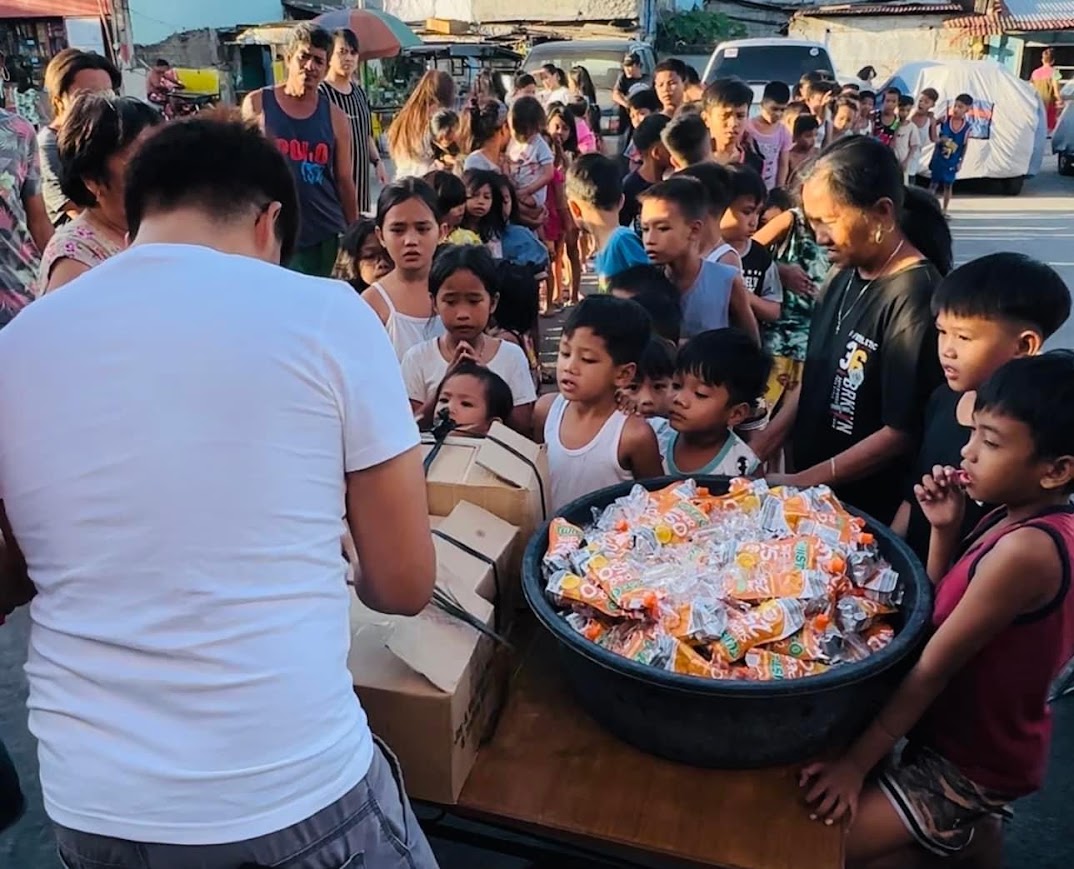 A young volunteer at the table, the first children lined up behind the bucket.