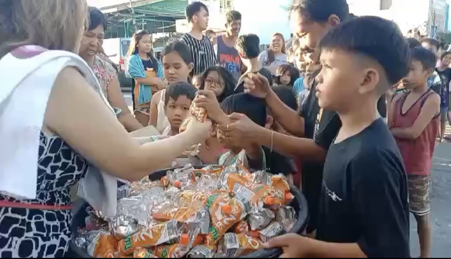 A juice pouch from the bucket, children waiting on both sides.