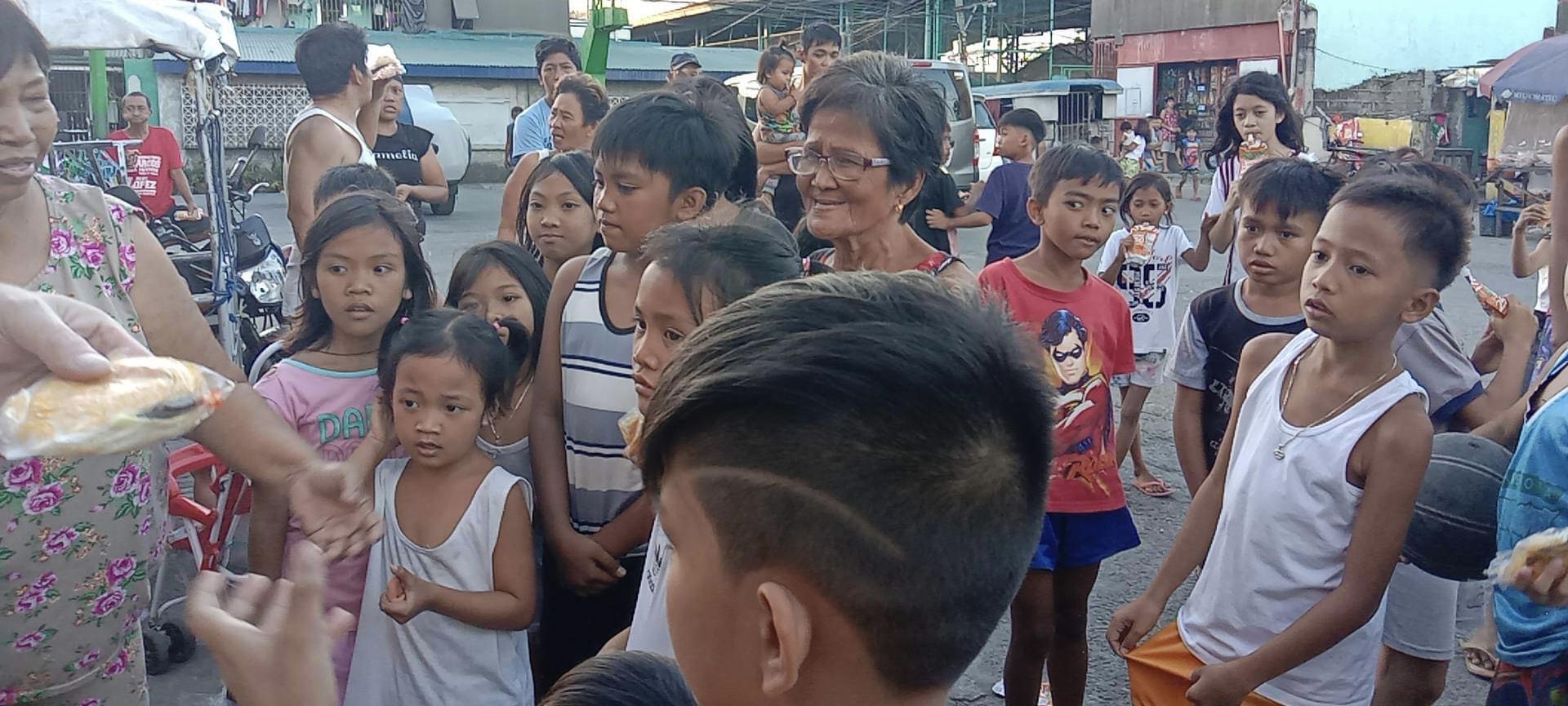A team member hands snacks to a small girl, an elder watching beside her.