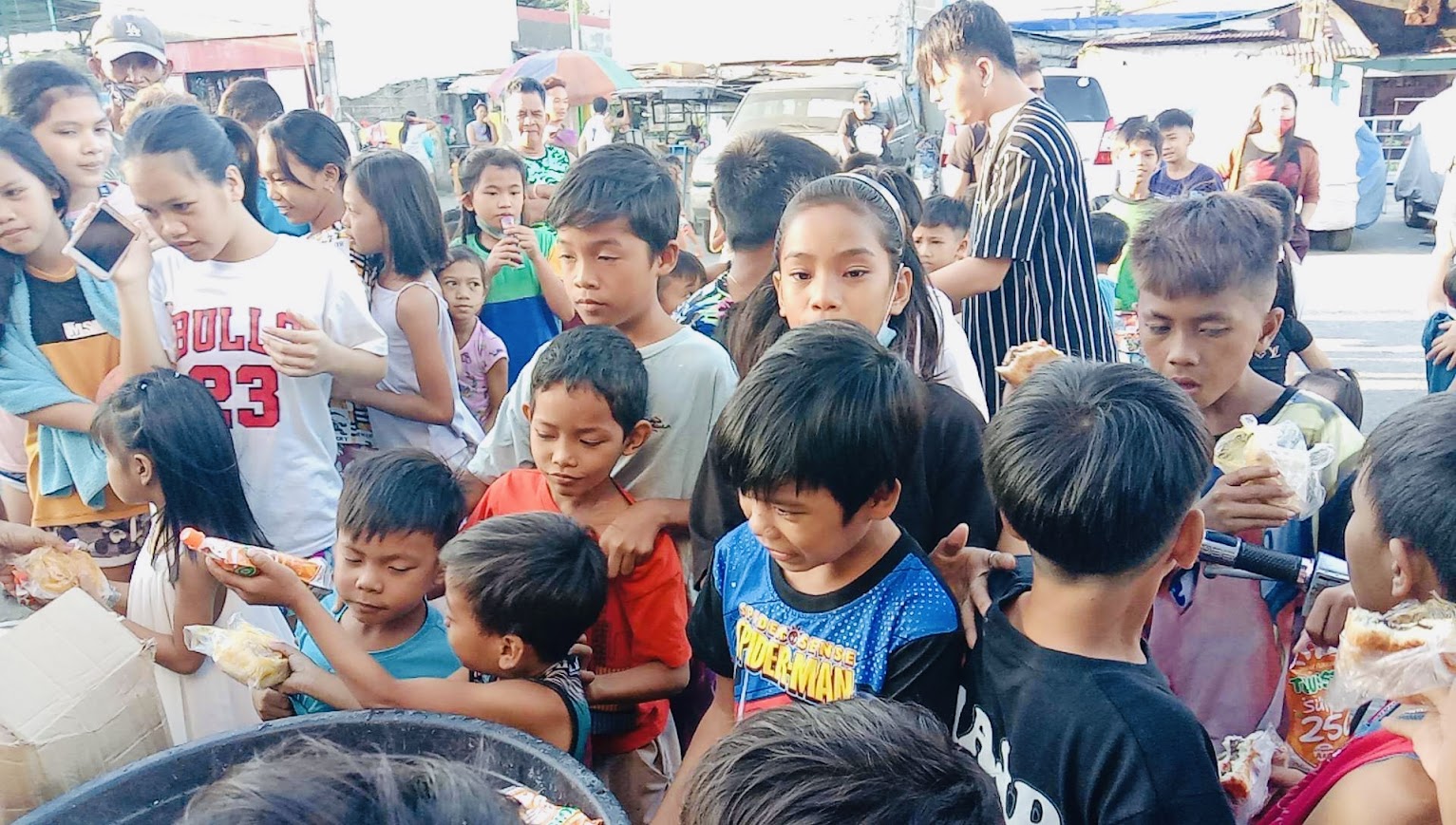 The crowd of children around the bucket, most already holding bread.