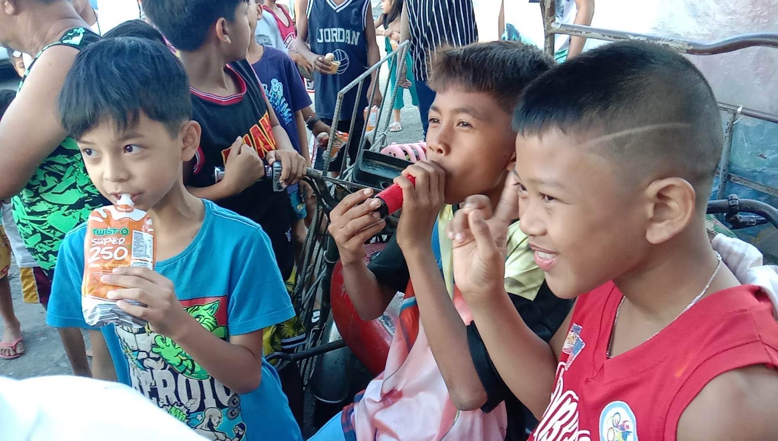 Three boys with their juice, sitting on a tricycle.