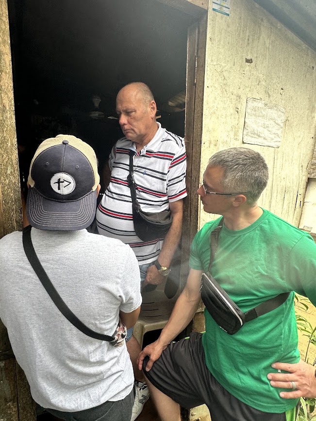 A team member prays over a woman outside her home, a partner volunteer beside her.