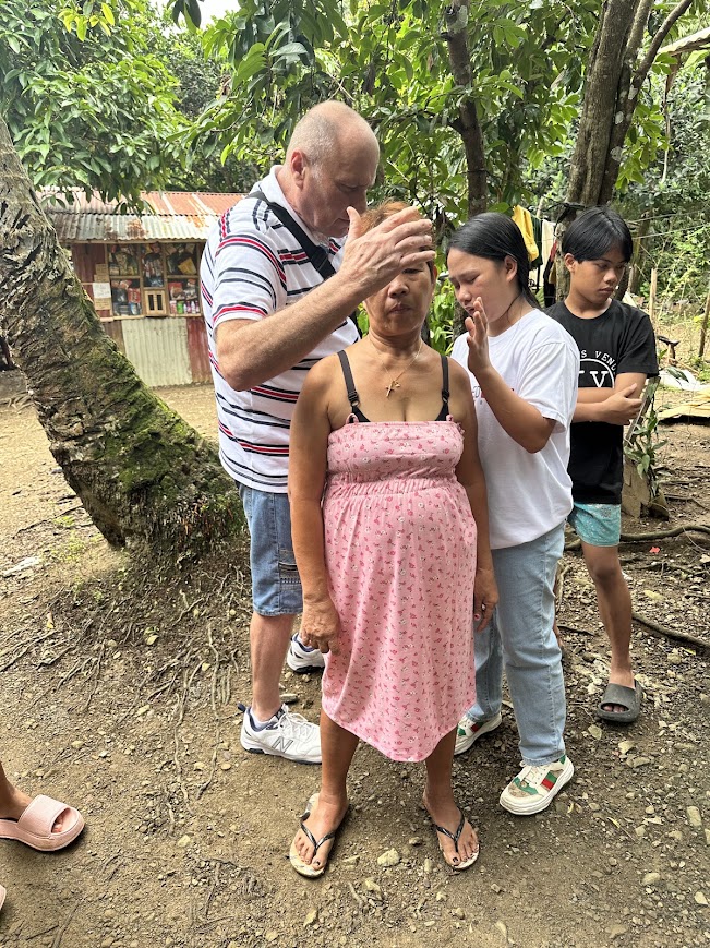 A team member prays with two teenagers at their doorway, heads bowed.