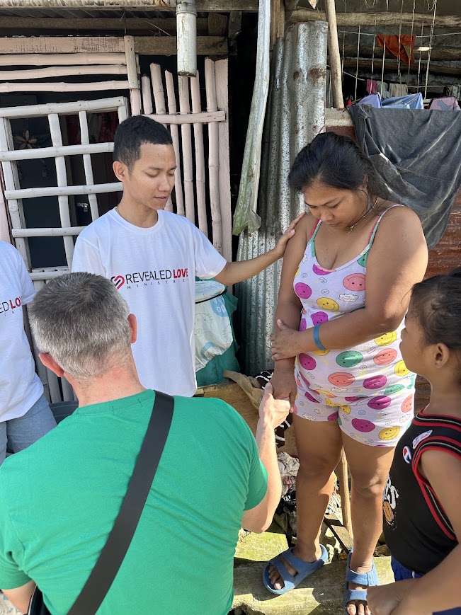 A partner volunteer and a team member pray with a mother outside her home.