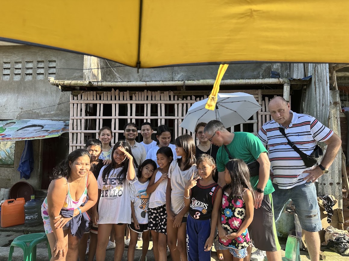 The family and team under a yellow umbrella, a girl flashing a peace sign.