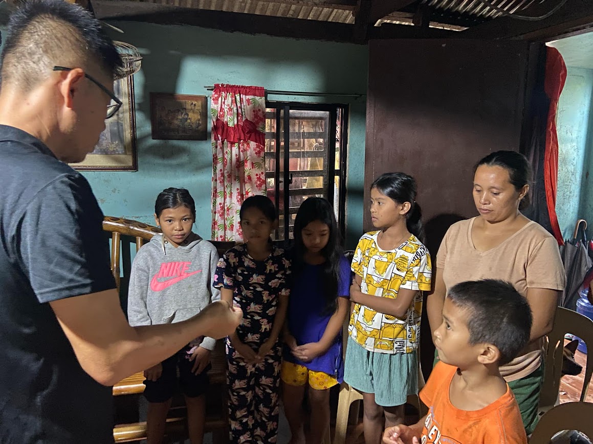 A leader prays with four girls and their mother in the living room.