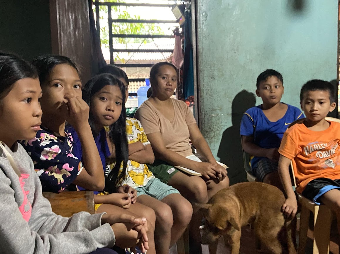 The children and their mother seated along the wall, a dog at their feet.