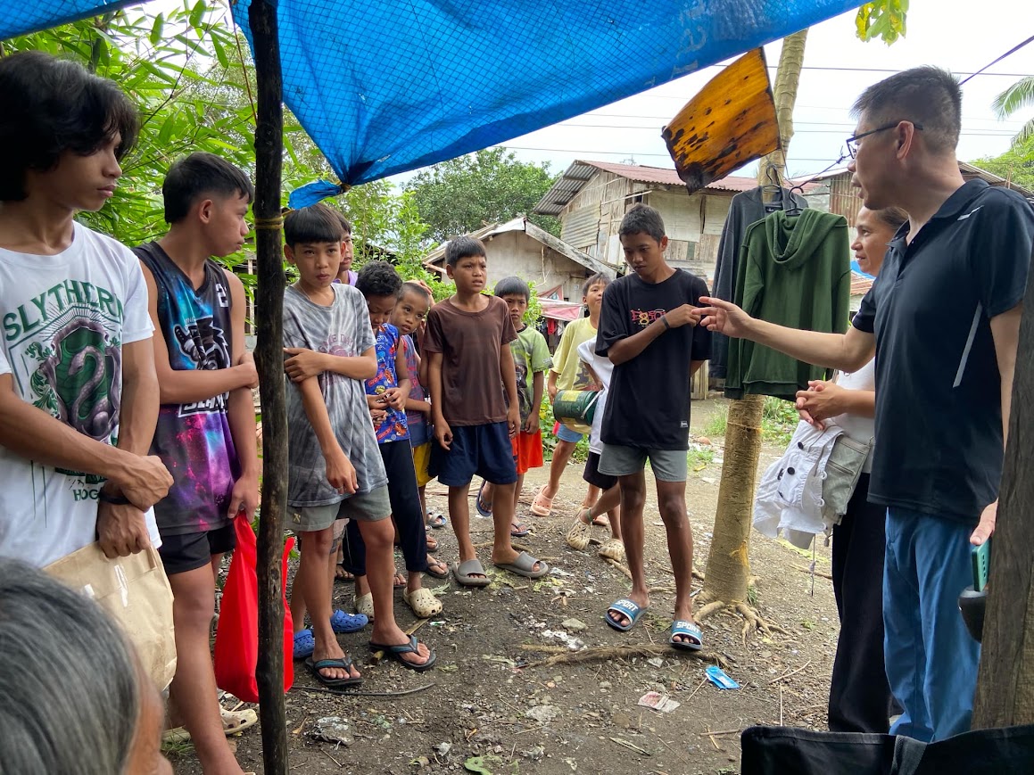 A leader speaks with a group of boys gathered under the blue tarp.