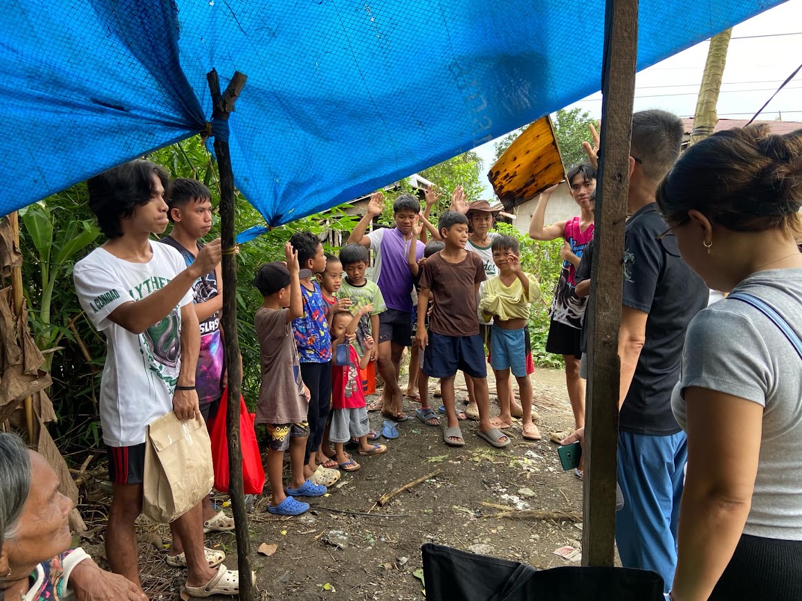 Hands go up among the children under the tarp.