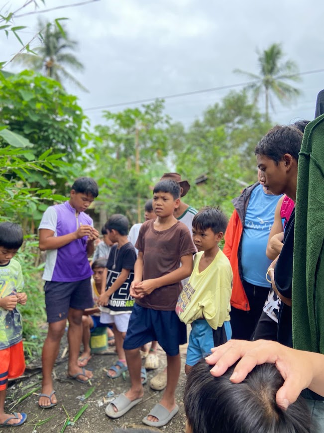 A hand rests on a child's head in prayer as the boys look on.
