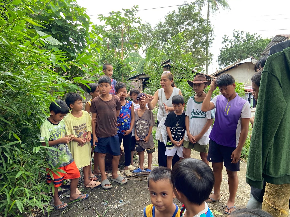 A team member speaks with the boys along the path, banana trees behind.
