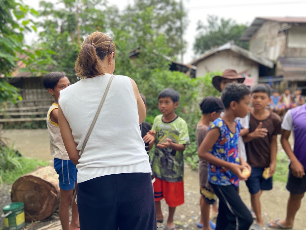 A team member talks with the boys, houses of the barangay behind.