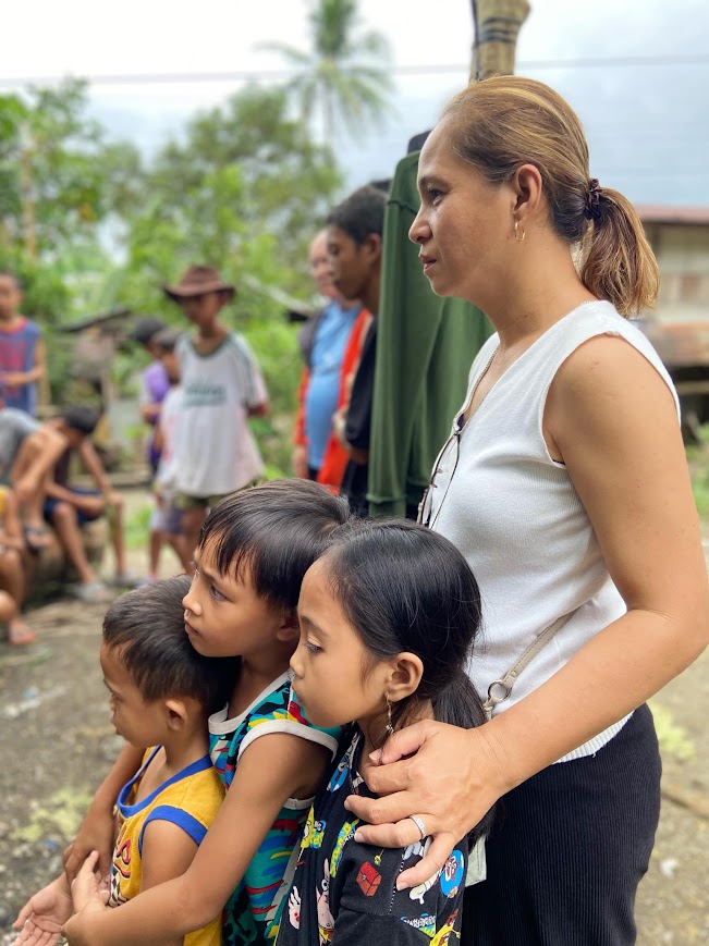 A team member holds three small children close as the group listens.