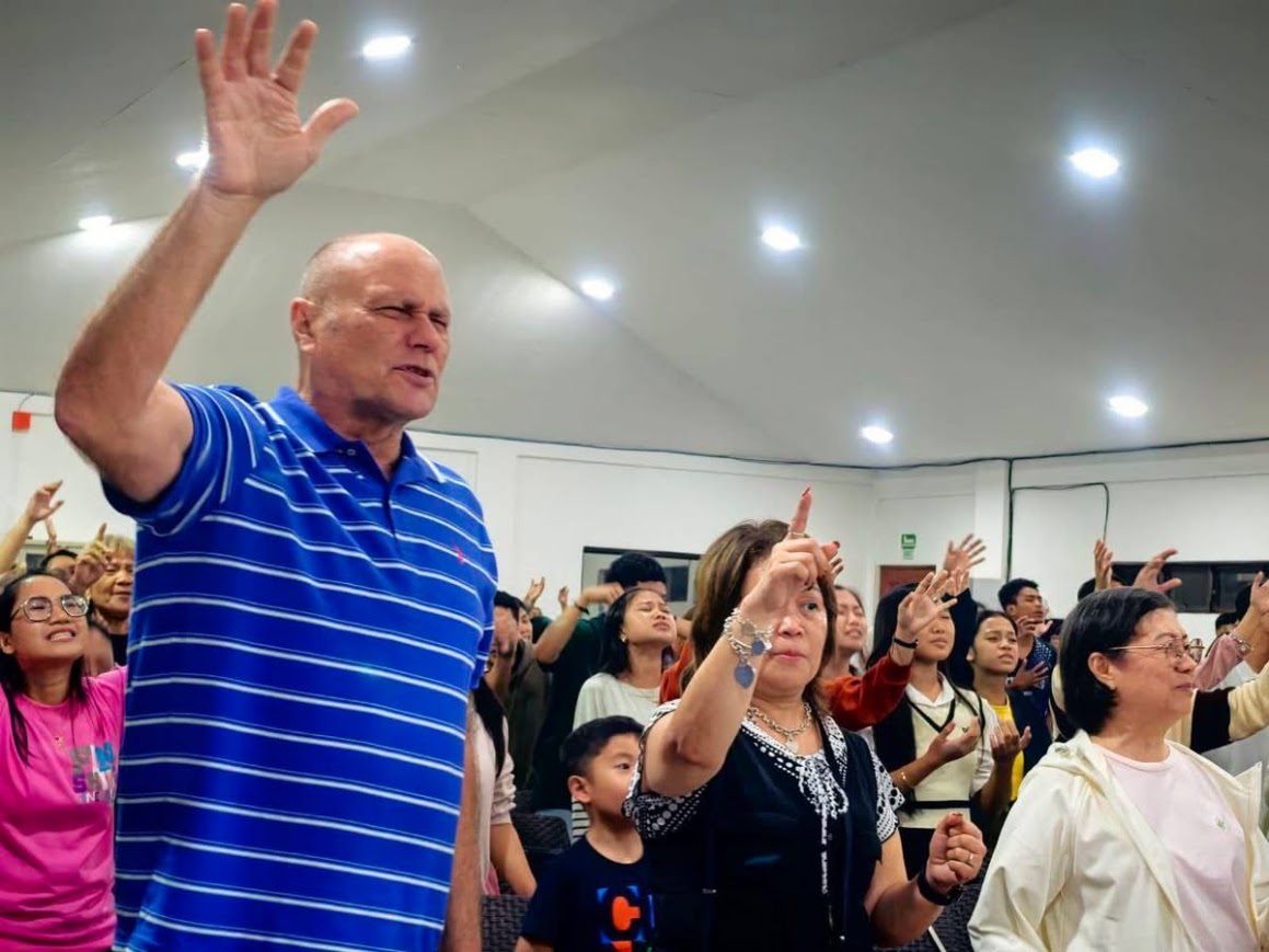 Worship — a ministry leader with hand raised, the crowd's hands up behind him.